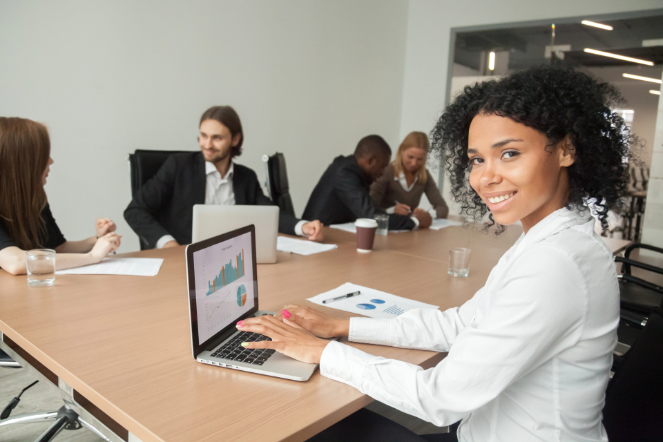 Smiling businesswoman using laptop for outsourced sales management support, improving sales performance and accountability in business.